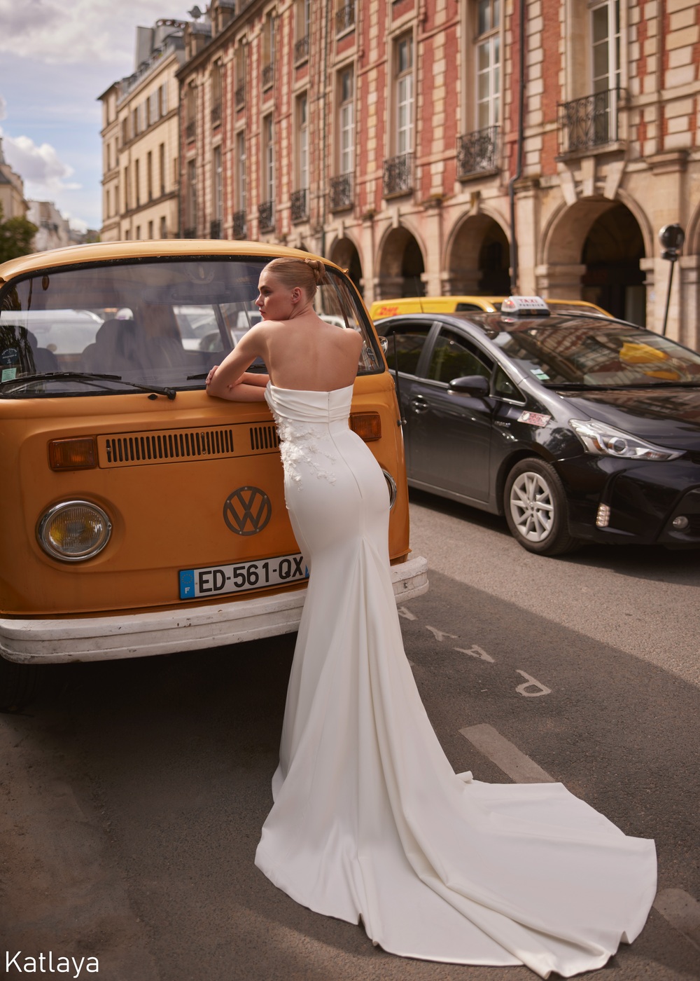 Bride wearing a modern strapless fitted wedding dress with a long train, leaning against a vintage van on a city street near Liverpool, from The White Gallery Ramsbottom.